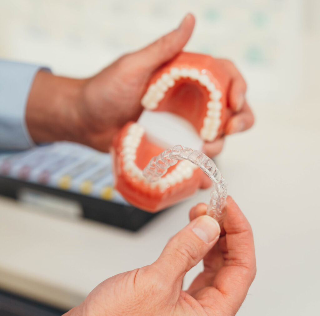 Orthodontist holding a clear removable retainer in front of a dental model showing aligned teeth