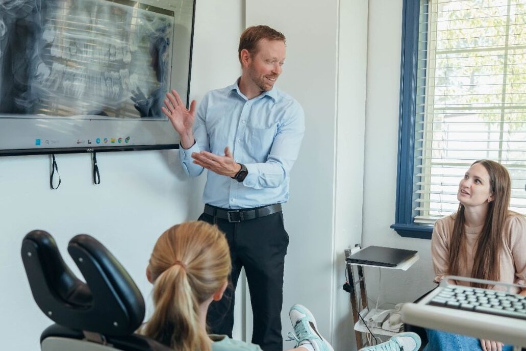 Orthodontist explaining a patient’s dental X-ray on a screen.